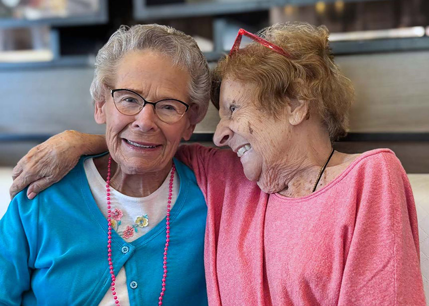 Two senior women embrace, sharing companionship and a joyful moment.