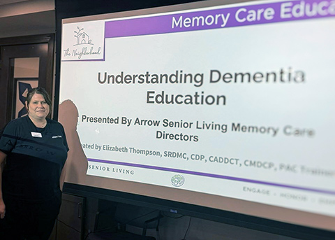 A CedarStone Senior Living team member stands beside a presentation reading "Understanding Dementia".