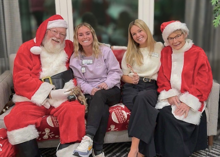 Two team members smile with Santa and Mrs. Claus.