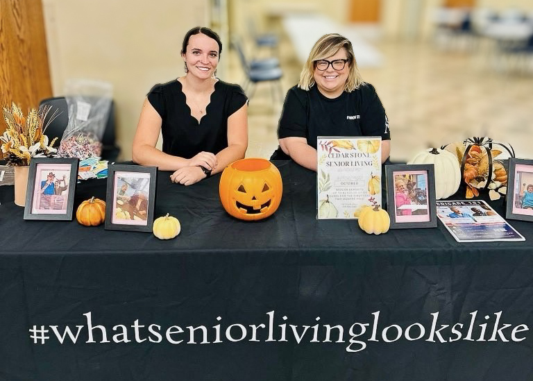 Two Arrow Senior Living team members seated at a table reading #whatseniorlivinglookslike