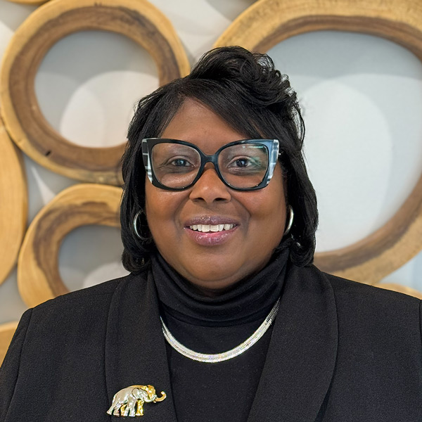 Youlanda Robinson, Business Office Director at CedarStone Senior Living, smiling in a professional headshot, wearing black attire and glasses, with a decorative circular wall backdrop.